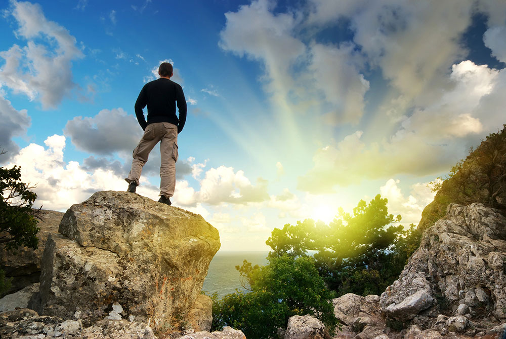 Man standing on a boulder looking away from the camera toward the horizon