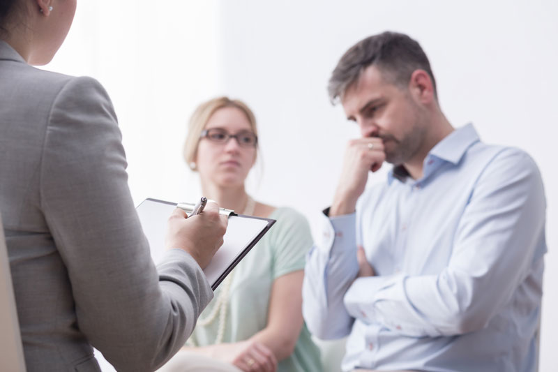 Man looking frustrated, woman looking at man, a third woman taking notes